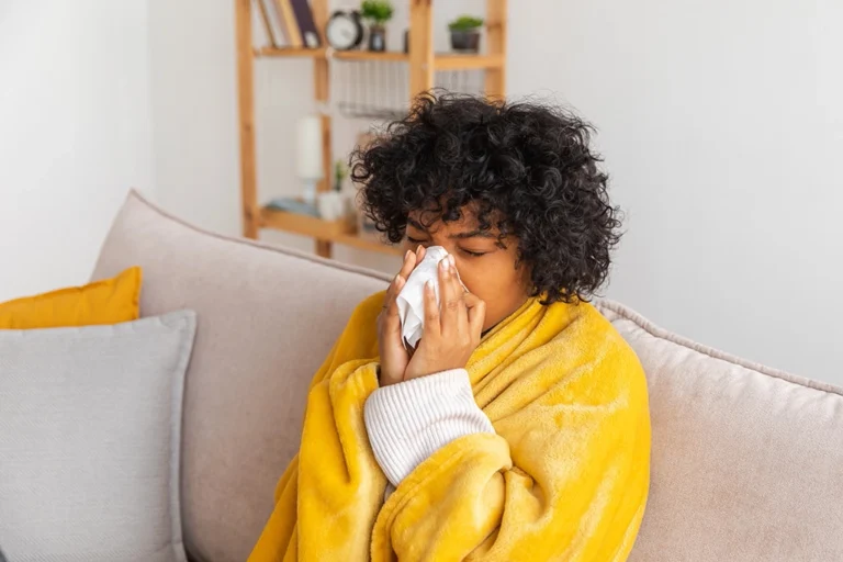 Young Woman Blowing Nose With Blanket On After Experiencing Sinus Problems